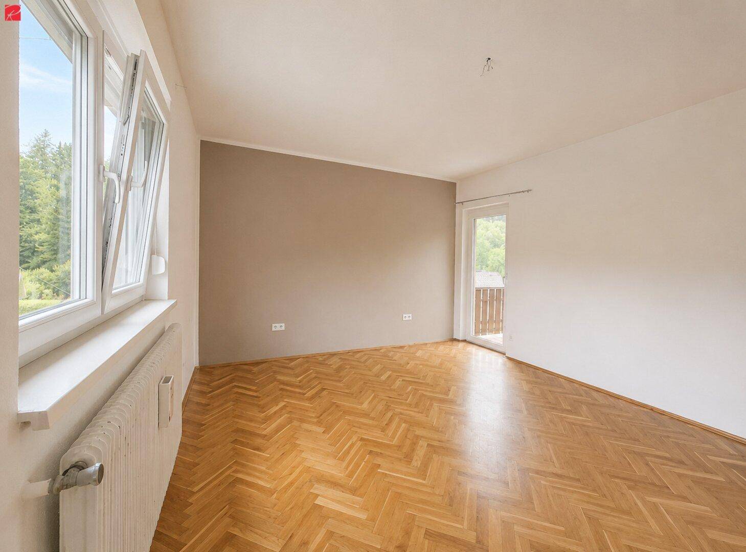Helles Zimmer mit Fischgrätparkett, einer Akzentwand und Zugang zu einem Balkon.