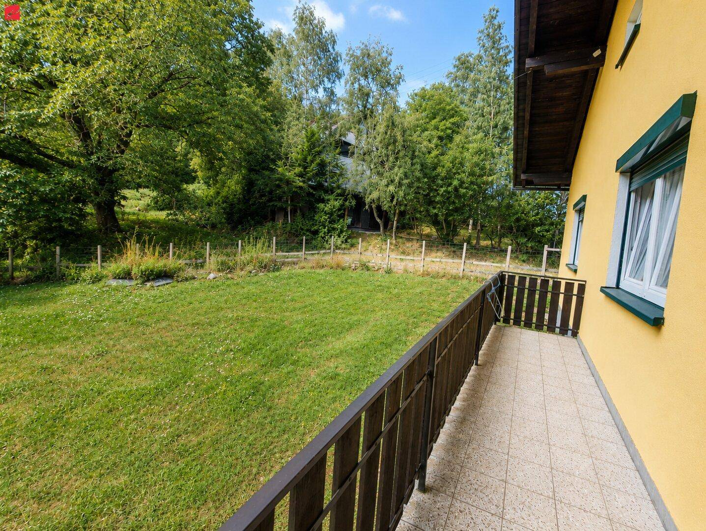 Balkon mit Fliesenboden und Holzbalkongeländer, bietet einen Blick auf den Garten und die Natur.