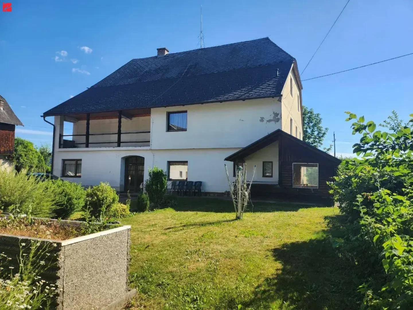 Rückseite eines weißen Gebäudes mit Balkon und einem gepflegten Gartenbereich mit Rasen und Pflanzen.