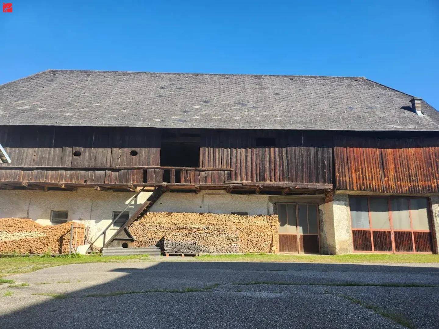 Großes Scheunengebäude mit Holzfassade und großen Stapeln Brennholz im Außenbereich.