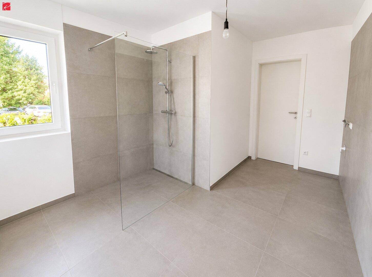 Modernes Badezimmer mit ebenerdiger Dusche, grauen Fliesen und einem Fenster für Tageslicht.
