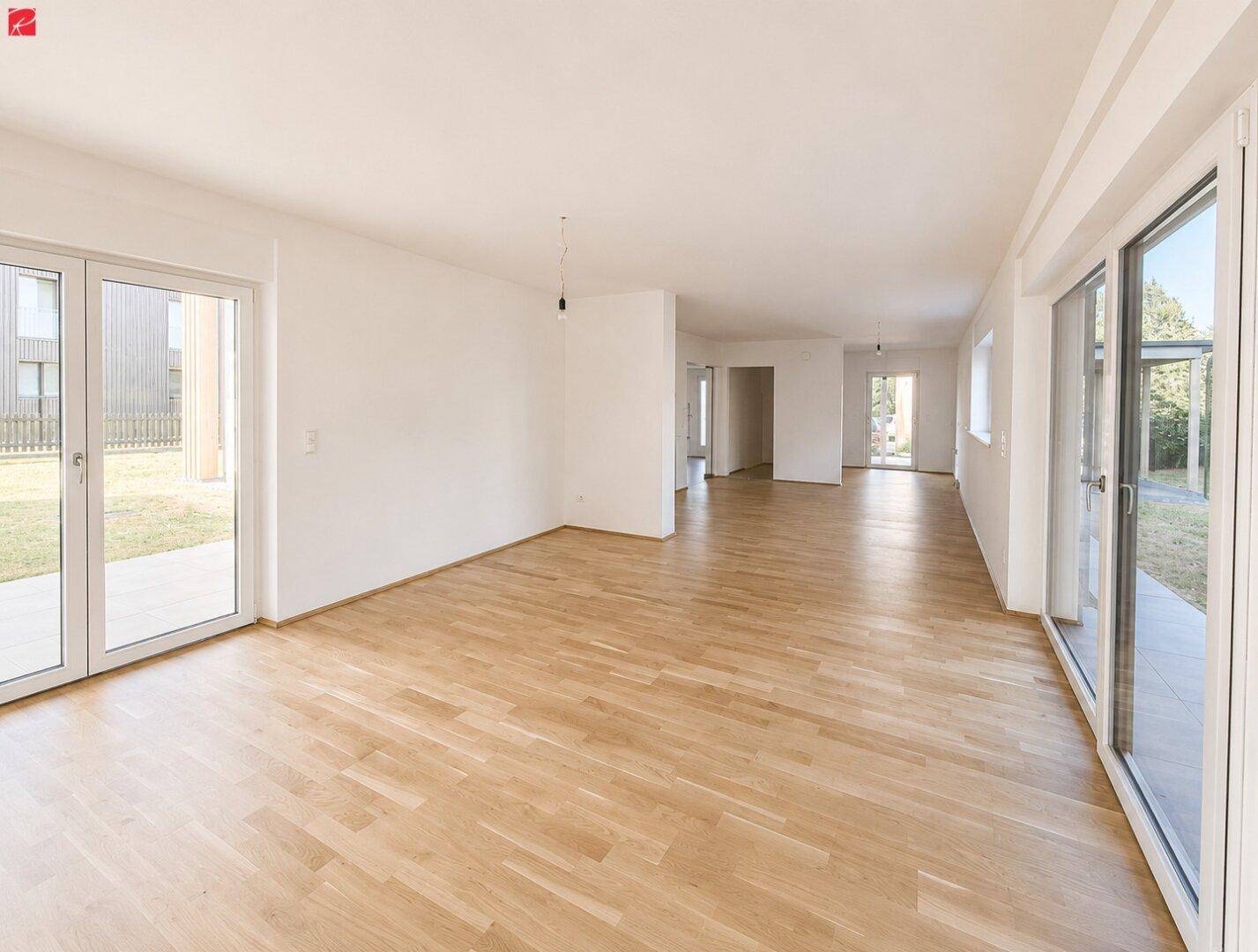Großzügiger, lichtdurchfluteter Wohnbereich mit Holzfußboden und großen Fensterfronten zum Garten.