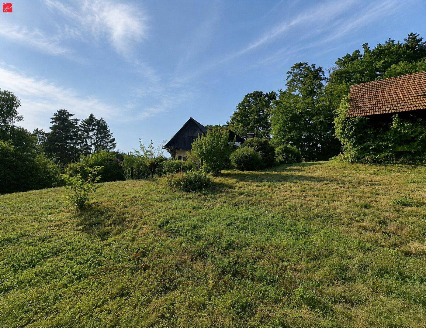 Weitläufiges Grundstück mit zwei Häusern, eingebettet in eine grüne Hügellandschaft unter blauem Himmel.