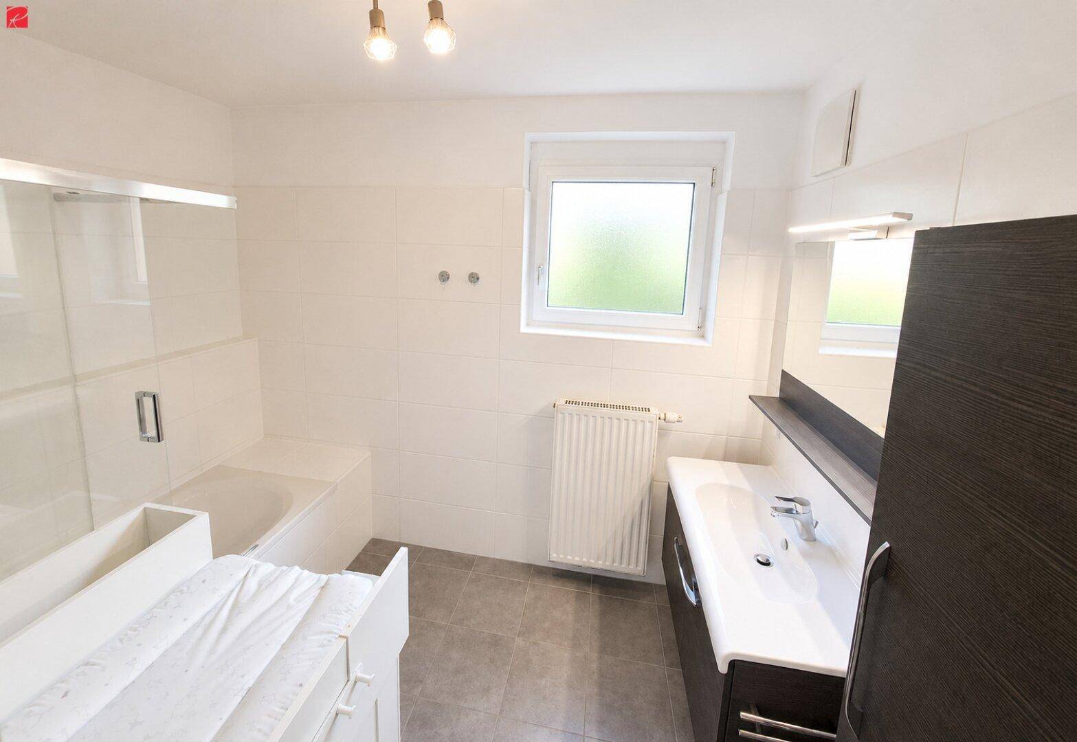 Modernes Badezimmer mit Badewanne, Einzelwaschbecken und Fenster für natürliches Licht.