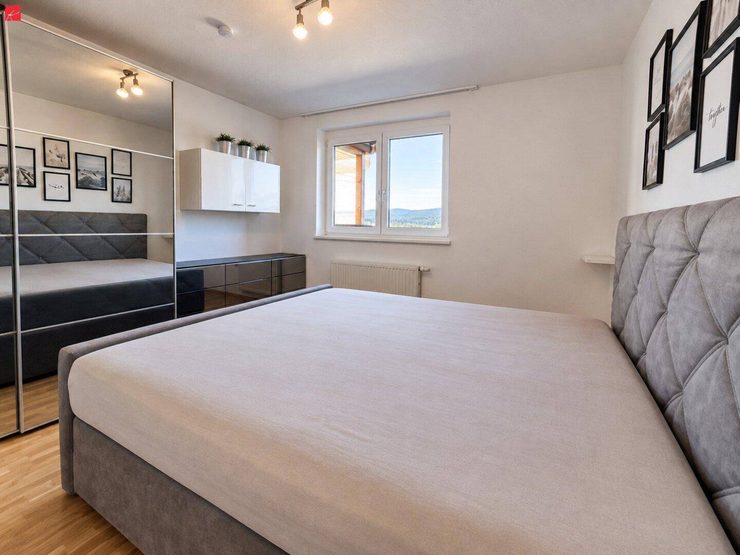 Schlafzimmer mit großem Bett, Spiegelschrank und Fenster mit Blick auf die umliegende Natur.