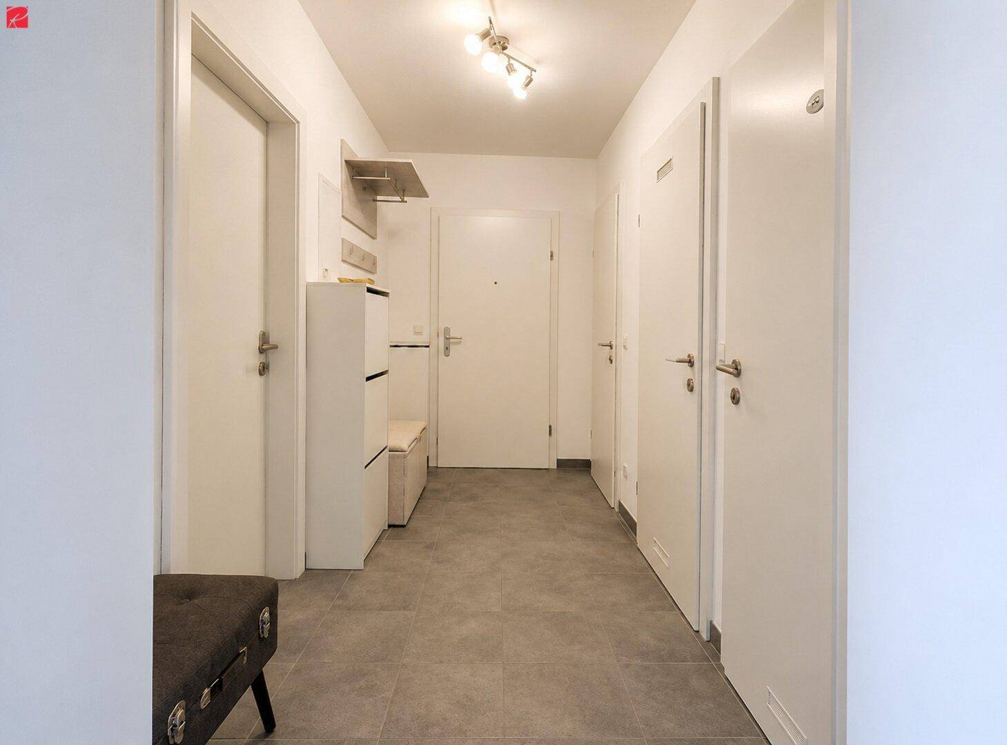 Heller Flur mit Fliesenboden und mehreren weißen Türen, ausgestattet mit einer kleinen Garderobe.