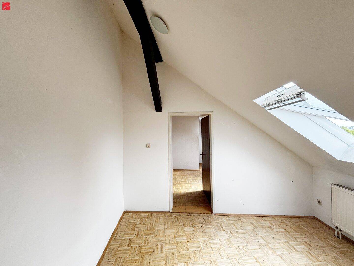 Leerer Dachbodenraum mit schrägen Wänden, Dachfenster und Holzboden.