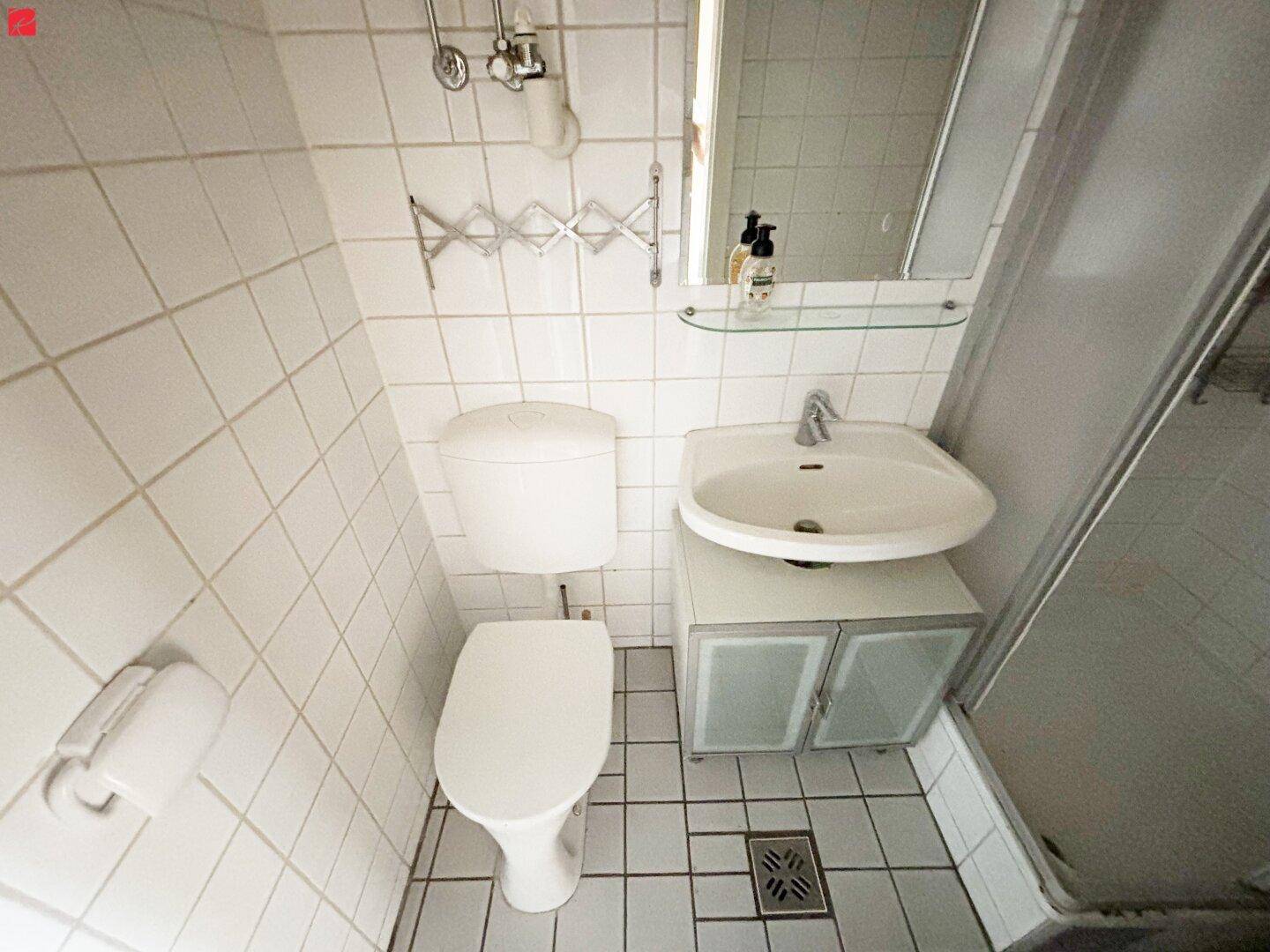 Kleines Badezimmer mit weißen Fliesen, Toilette, Waschbecken und Duschkabine.