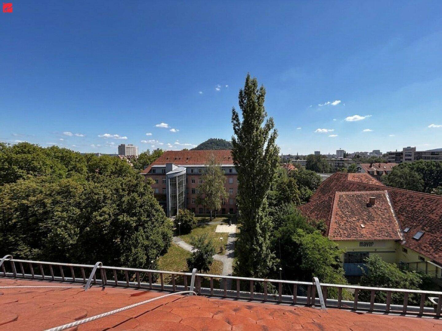 Weitläufiger Blick über die Stadt und grüne Bäume von einem Dach mit Ziegeln.