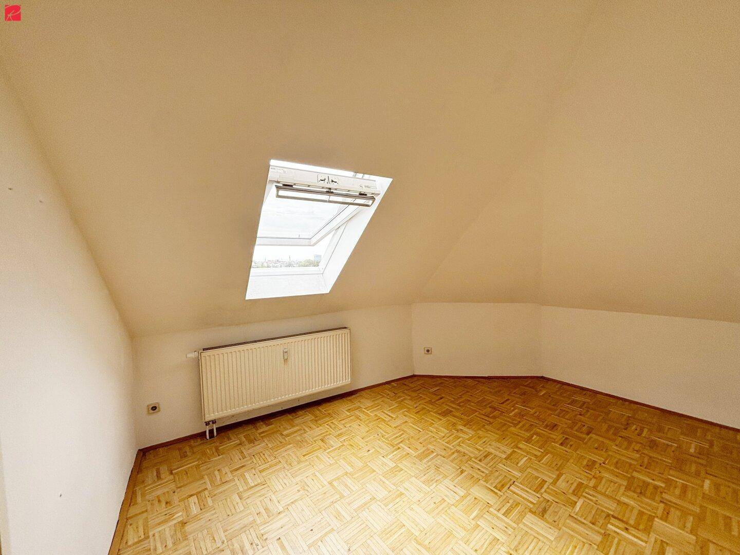 Leerer Dachbodenraum mit schrägen Wänden, Dachfenster und Heizkörper.