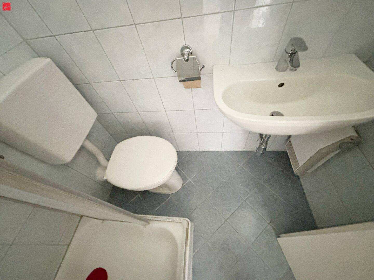 Kleines Badezimmer mit WC, Waschbecken und Duschkabine, komplett gefliest.