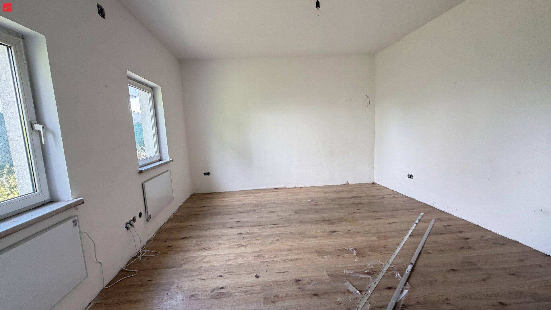 Heller, unmöblierter Raum mit neuem Holzplankenboden und zwei Fenstern mit Heizkörpern.