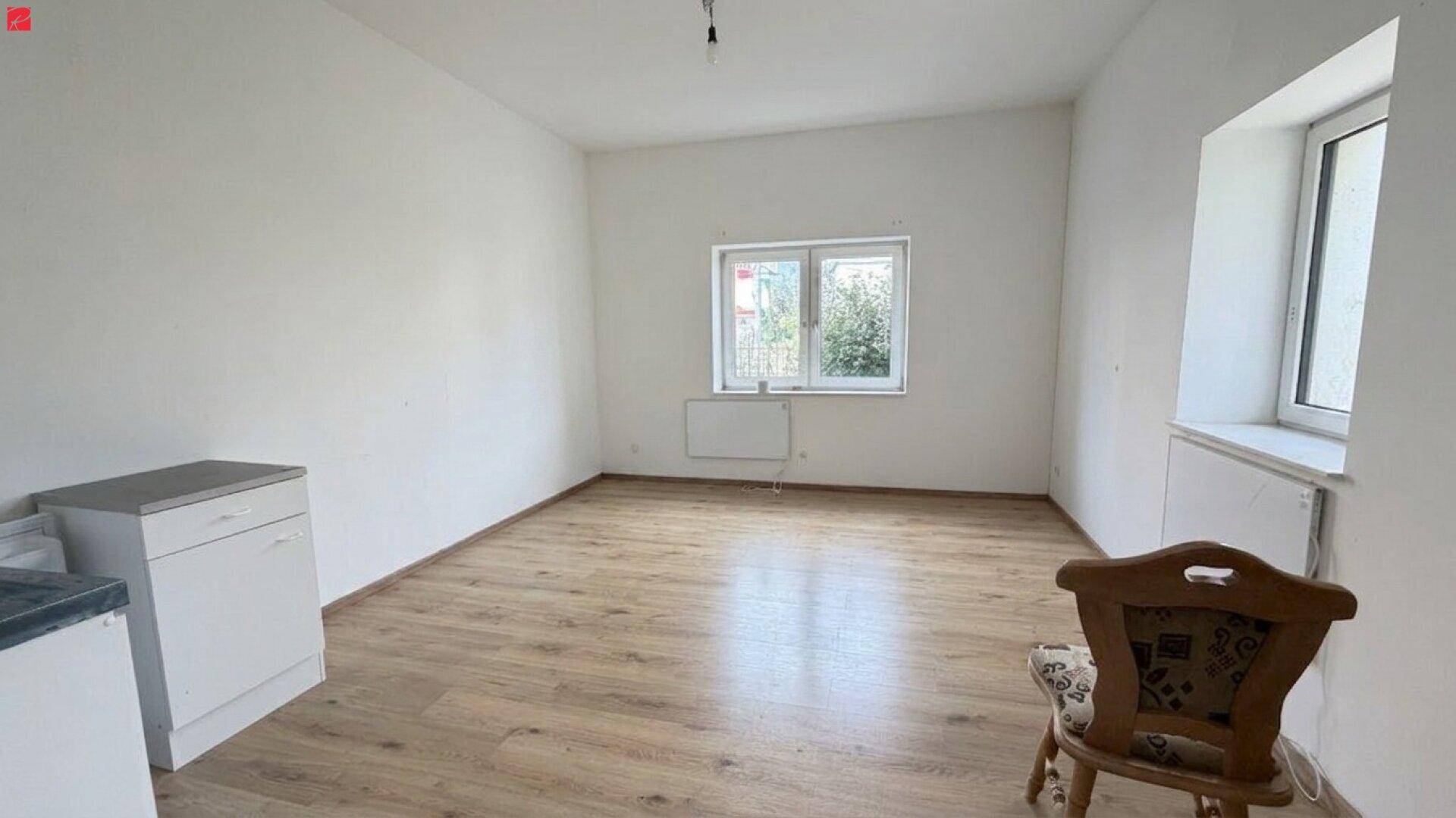 Unmöblierter Raum mit Holzplankenboden, Fenster und einer einfachen Küchenzeile, bereit zur Gestaltung.