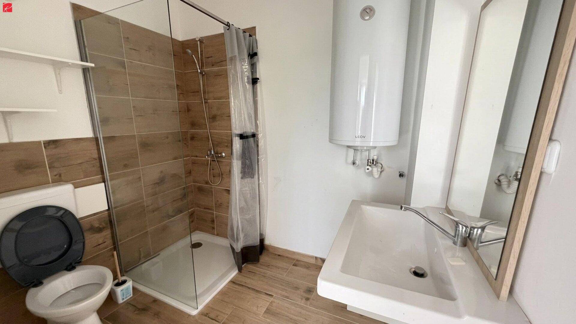 Modernes Badezimmer mit Duschkabine, WC, Waschbecken und Warmwasserboiler, in hellen Holztönen gefliest.