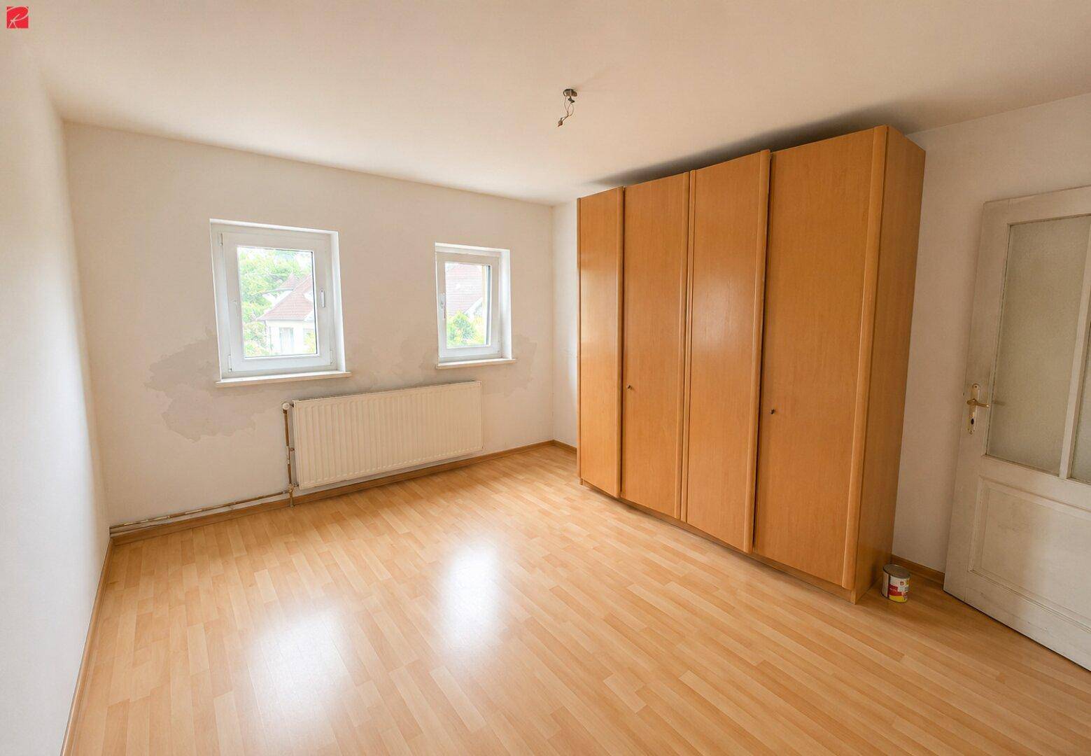 Helles Schlafzimmer mit Laminatboden, Einbauschrank und zwei Fenstern mit Blick ins Grüne.