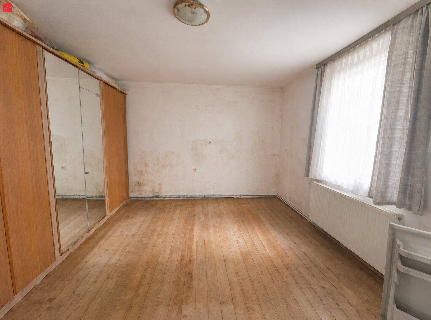 Geräumiges Schlafzimmer mit Dielenboden, Spiegelschrank und Fenster mit Vorhängen.