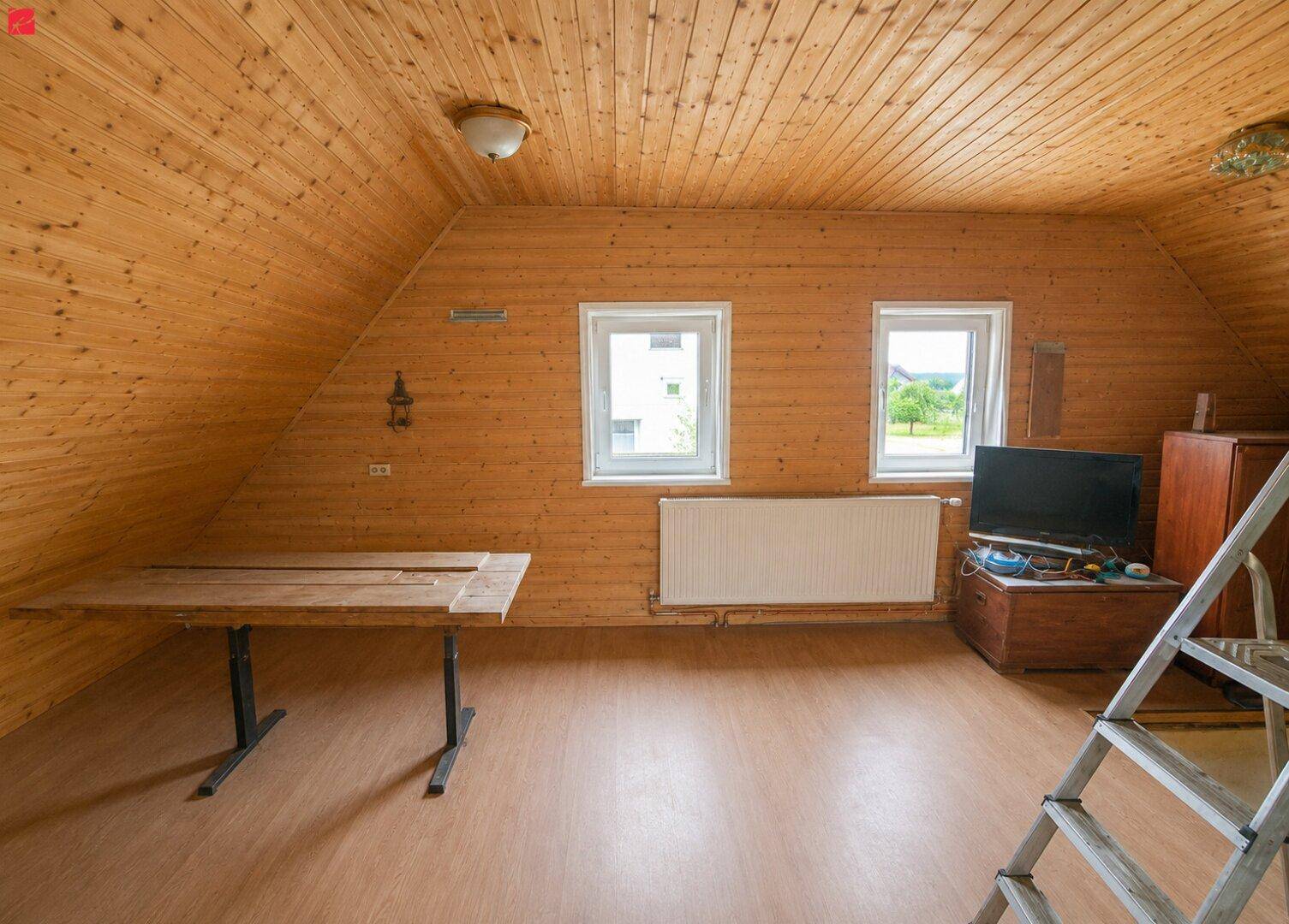 Gemütlicher Dachbodenraum mit Holzverkleidung, Laminatboden und zwei Fenstern.