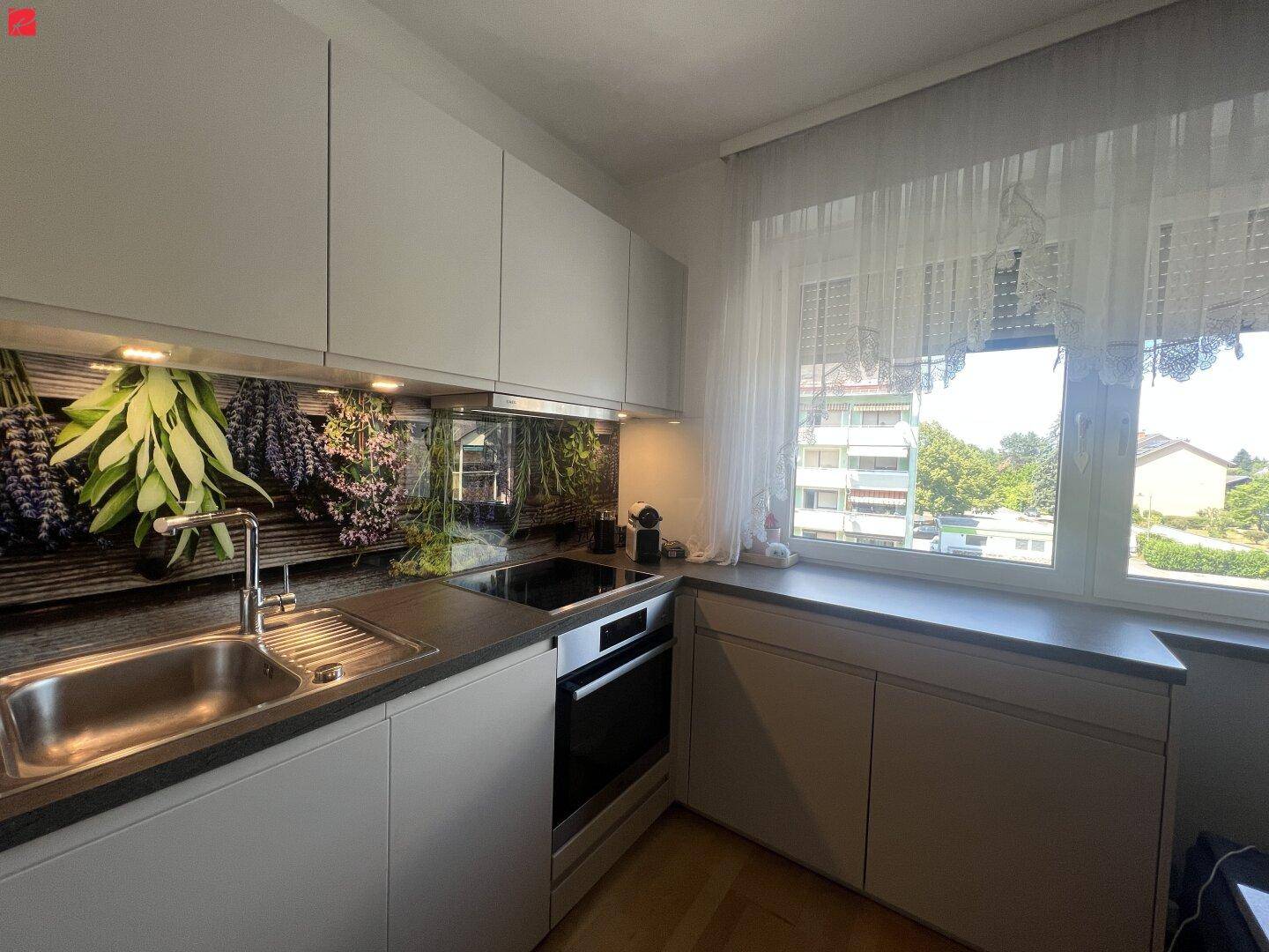 Moderne Einbauküche mit hellgrauen Schränken, dunkler Arbeitsplatte und einem Fenster mit Blick ins Grüne.