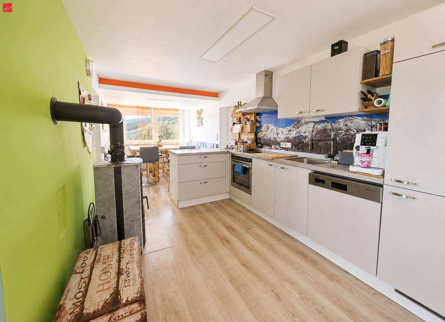 Helle, moderne Küche mit integrierten Geräten, Holzboden und Kachelofen im Hintergrund.