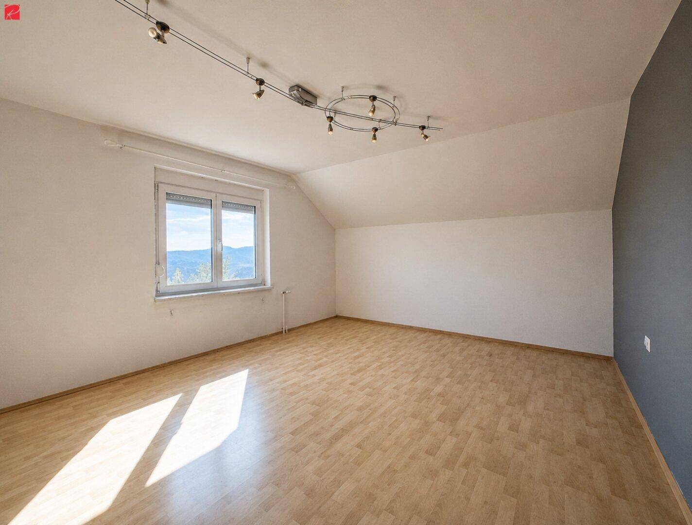 Geräumiges Schlafzimmer im Dachgeschoss mit Holzboden, Schrägdecke und Bergblick.