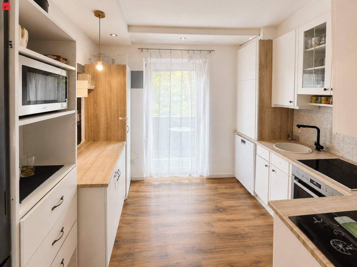 Funktionale Küche mit hellen Holz- und weißen Fronten, integrierten Geräten und Fenster.