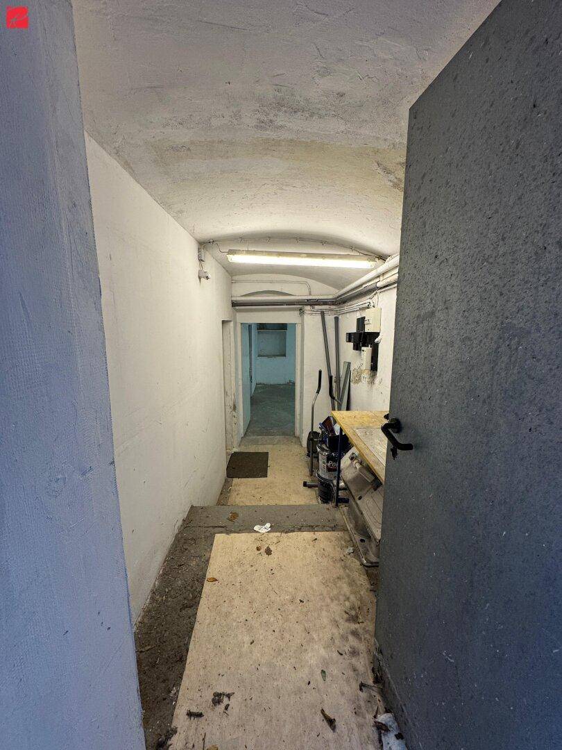 Schmaler Flur oder Treppenabgang zum Keller mit einfacher Beleuchtung und sichtbaren Rohren.