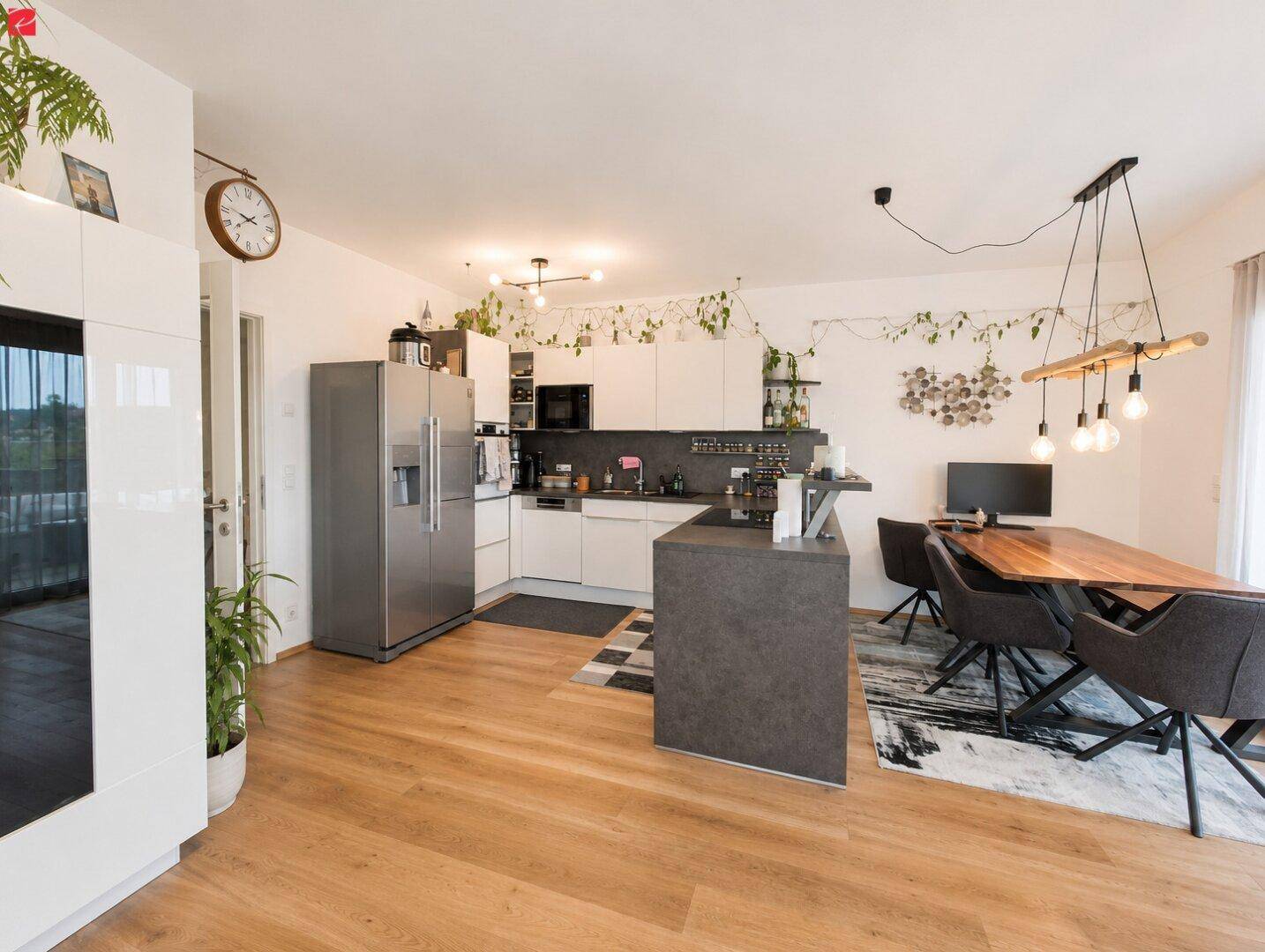 Heller offener Wohn-Essbereich mit moderner Einbauküche, Kücheninsel und Holzboden.