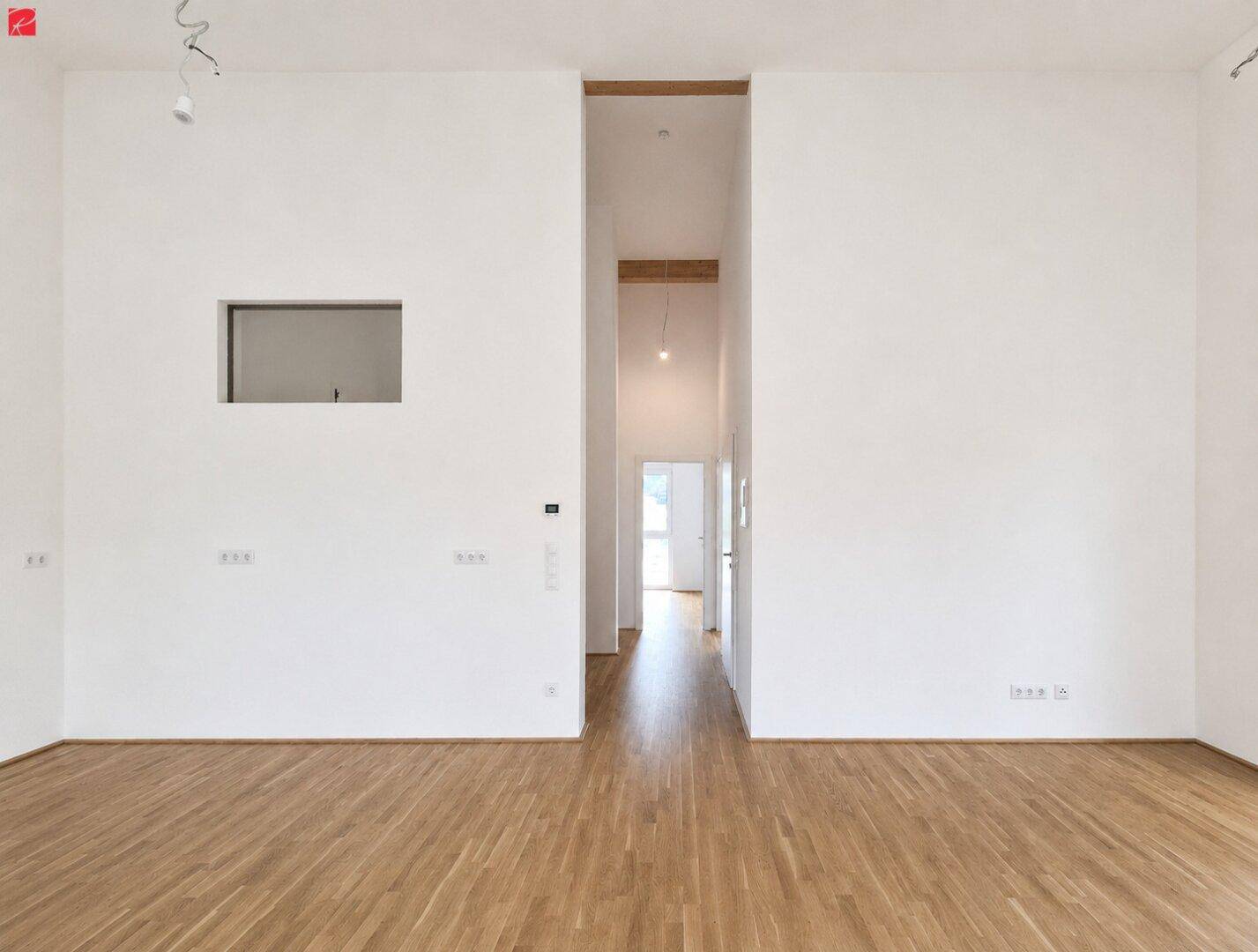 Großer, heller Raum mit Holzparkettboden und hohen Decken, der einen offenen Übergang zum Flur bietet.