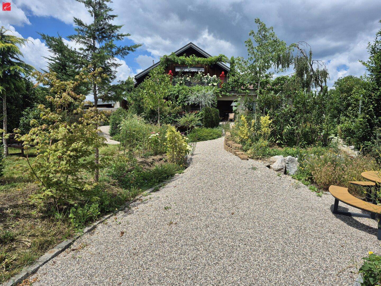 Einfamilienhaus mit weitläufigem Garten, Kiesweg und vielfältiger Bepflanzung an einem sonnigen Tag.