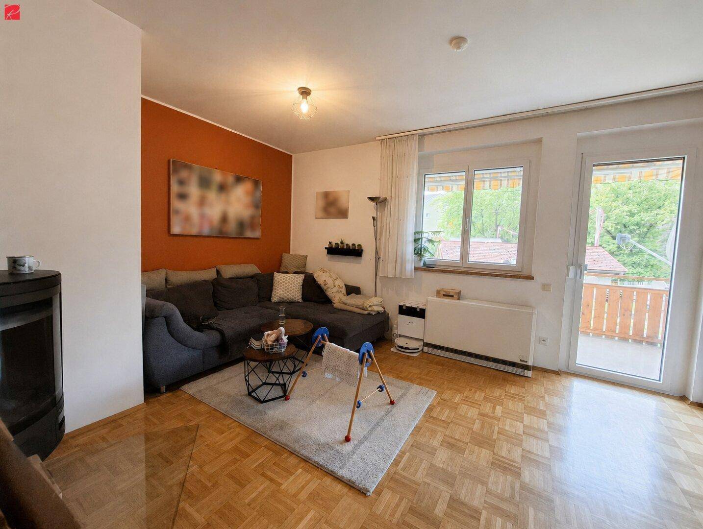 Helles Wohnzimmer mit gemütlichem Sofa, Kamin und Zugang zu einem Balkon mit Parkettboden.