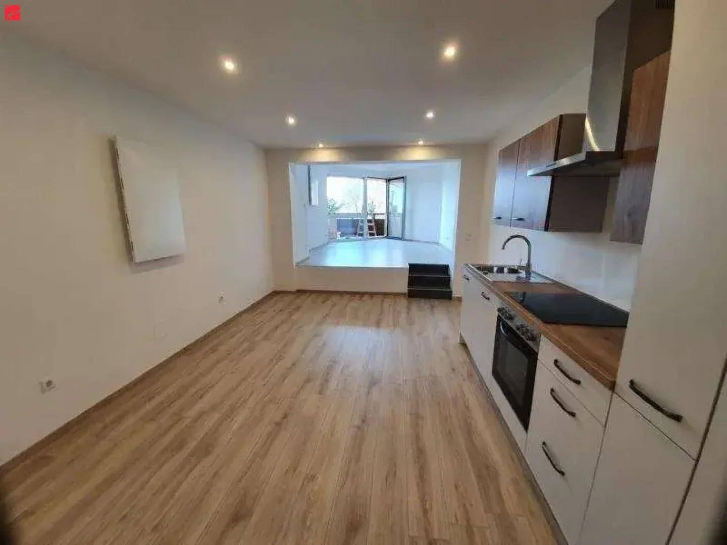 Heller offener Wohnbereich mit integrierter Küche, Laminatboden und Zugang zum Balkon.