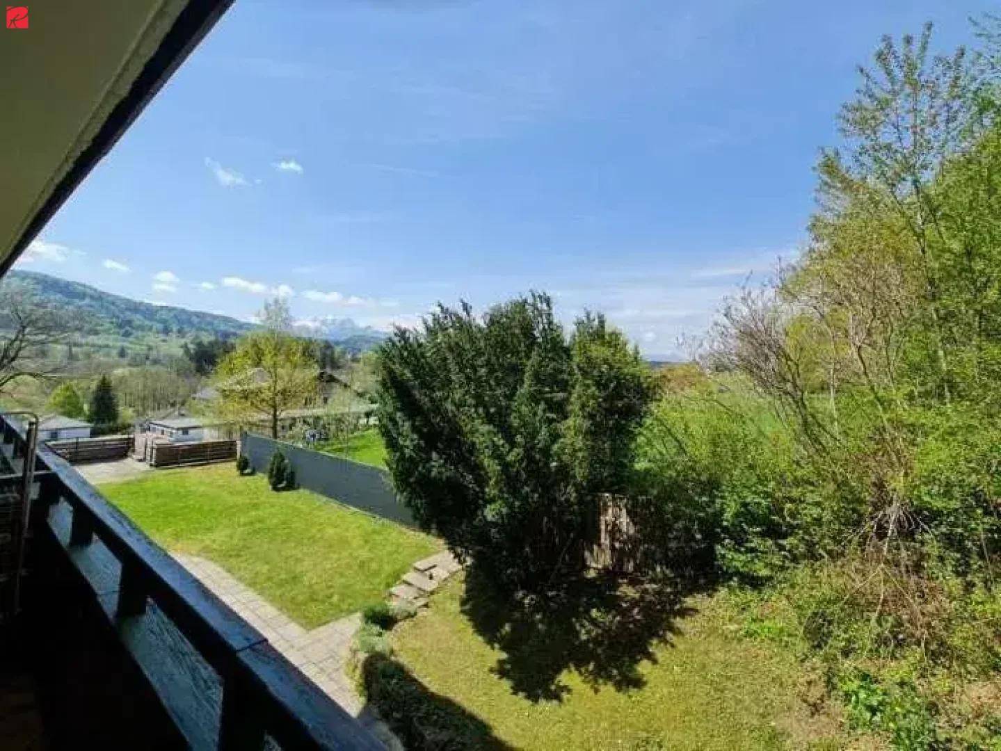 Balkon mit weitem Blick über grüne Felder, Bäume und die umliegende Berglandschaft.