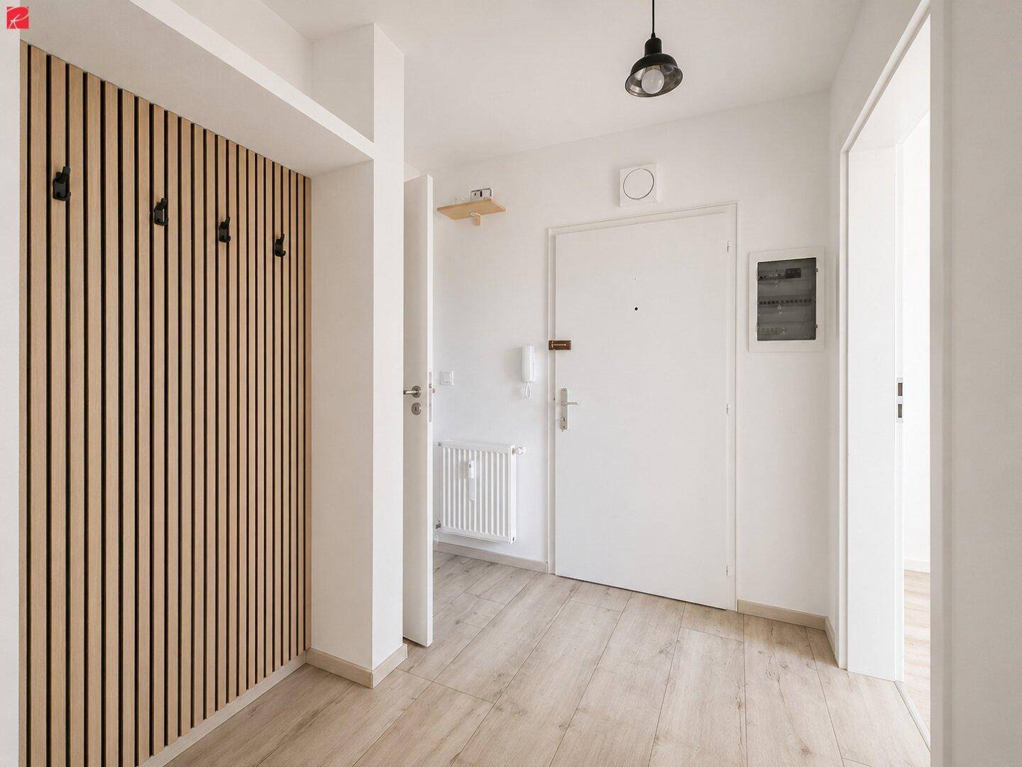 Heller Eingangsbereich mit Holzwandverkleidung und Garderobenhaken, führt zu weiteren Räumen.