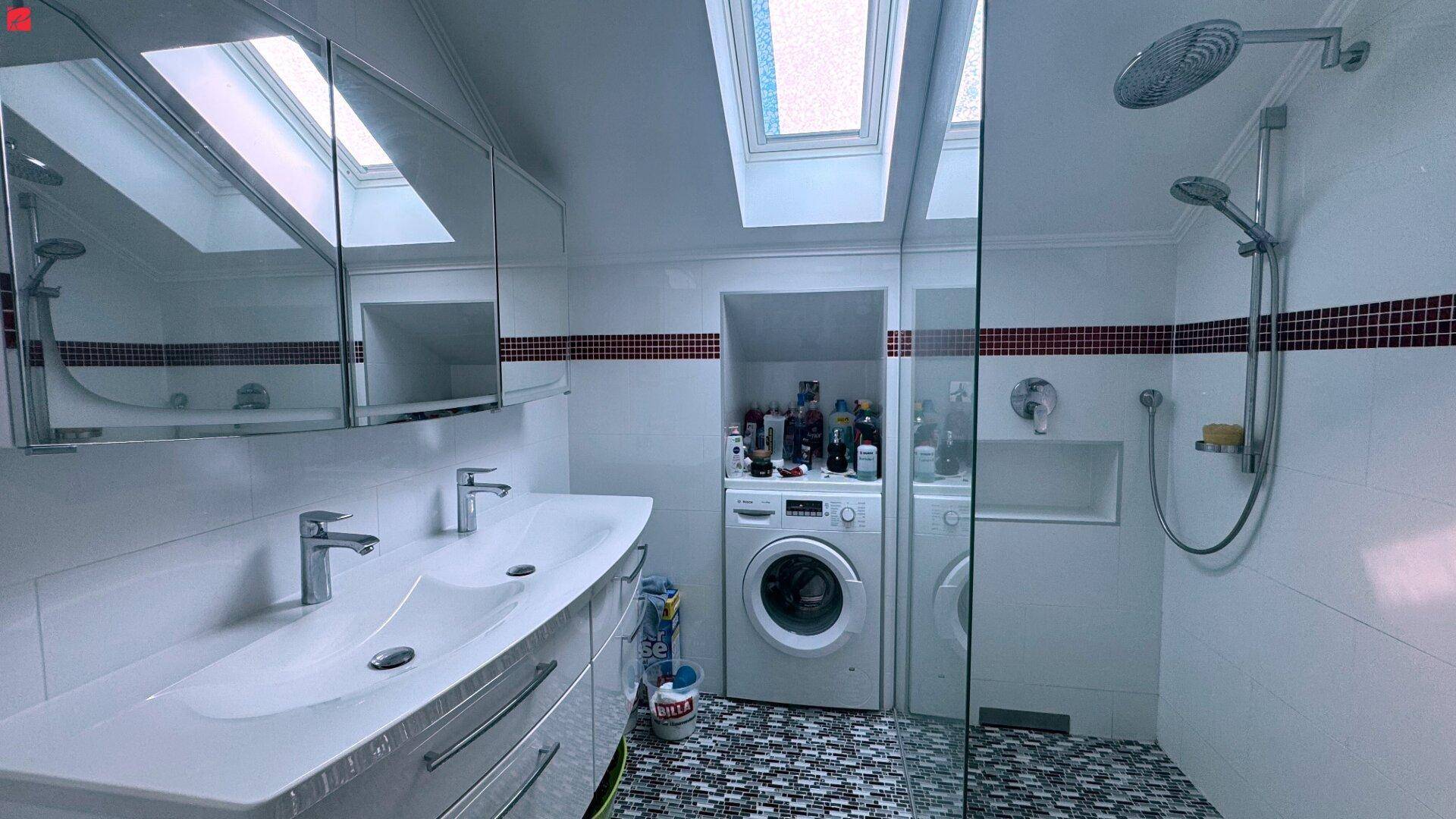 Helles Badezimmer im Dachgeschoss mit Doppelwaschbecken, moderner Dusche, Waschmaschine und Dachfenster.