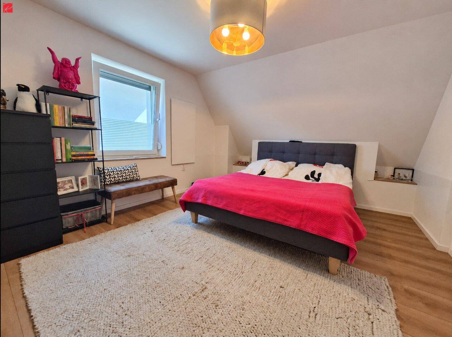 Gemütliches Schlafzimmer im Dachgeschoss mit schräger Decke, großem Bett und Teppichboden.