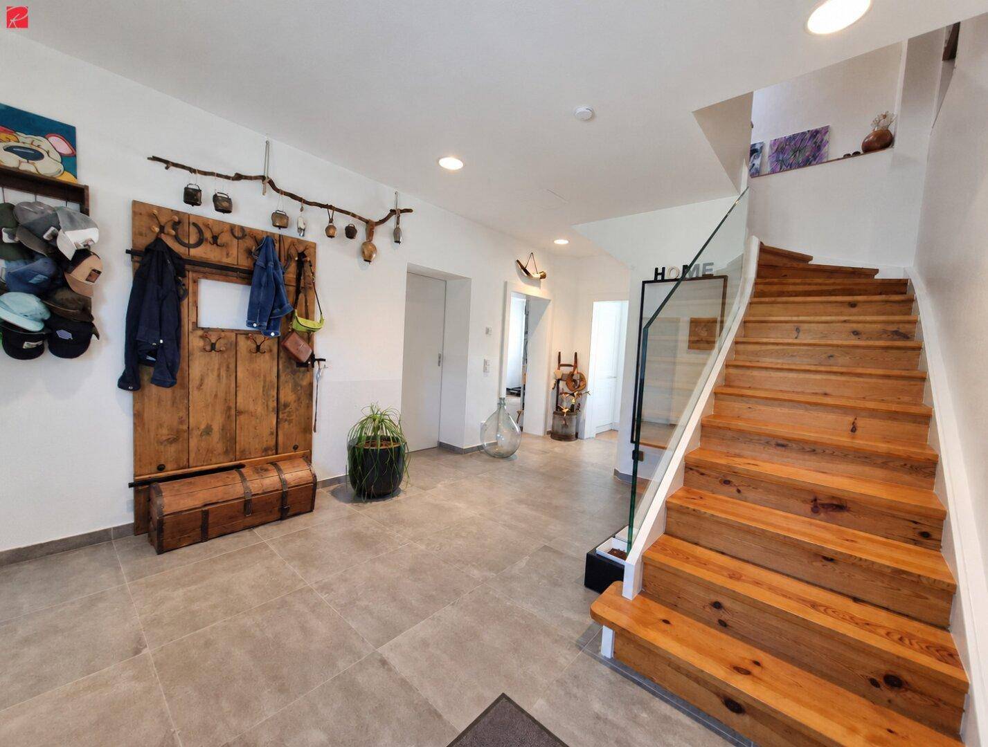 Geräumiger Eingangsbereich mit Holztreppe, Fliesenboden und rustikaler Garderobe.