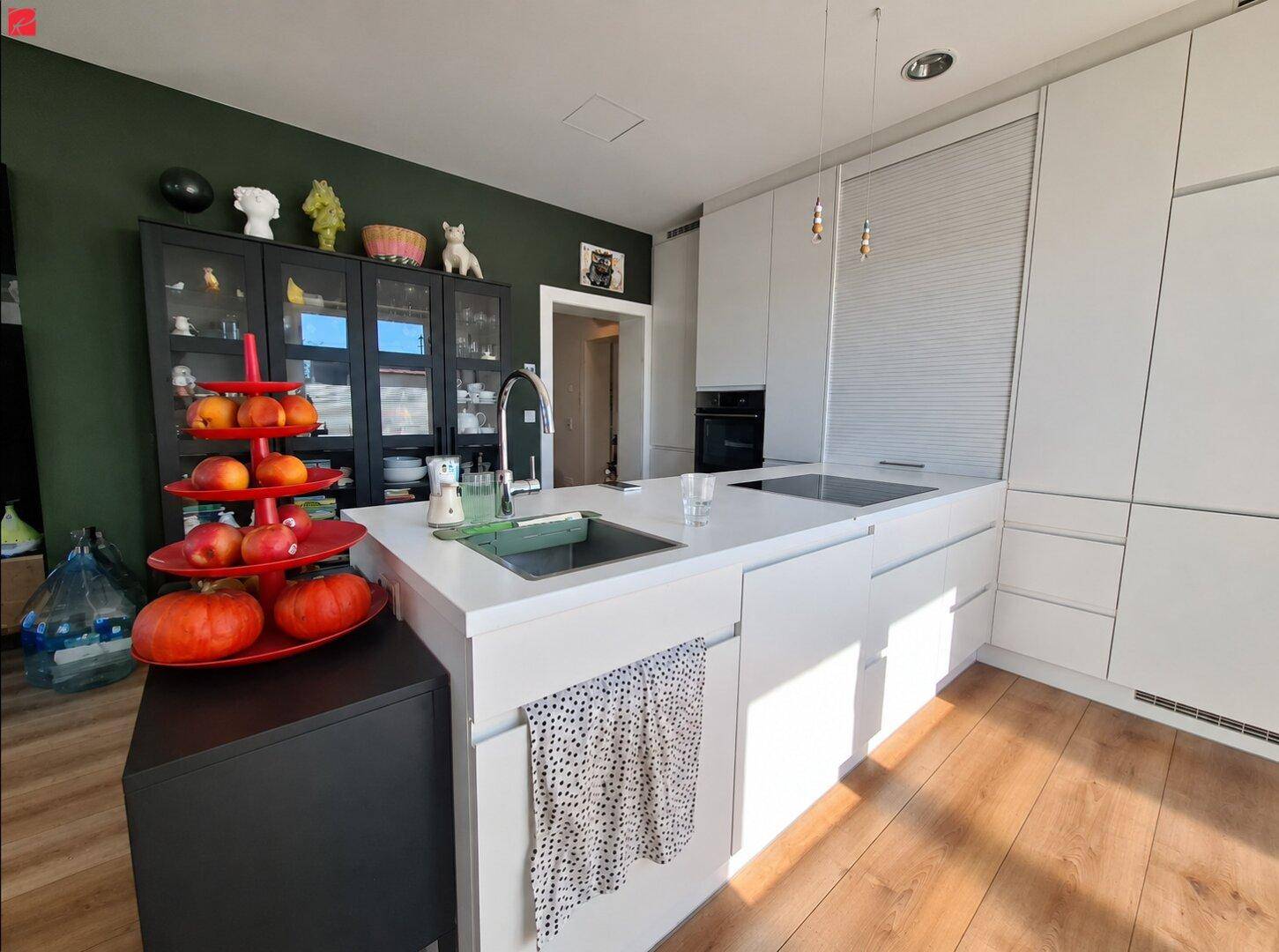 Moderne Küche mit weißer Kücheninsel, dunkler Wand und Holzboden, ausgestattet mit modernen Geräten.