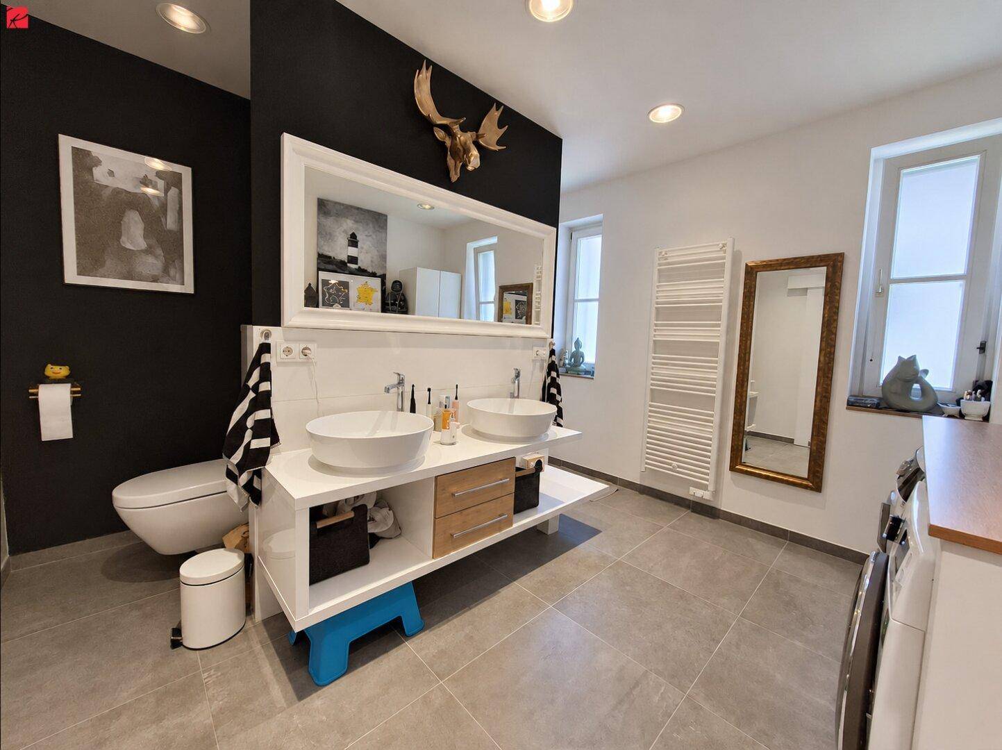 Modernes Badezimmer mit Doppelwaschbecken, großer Spiegelfläche und dunkler Akzentwand.