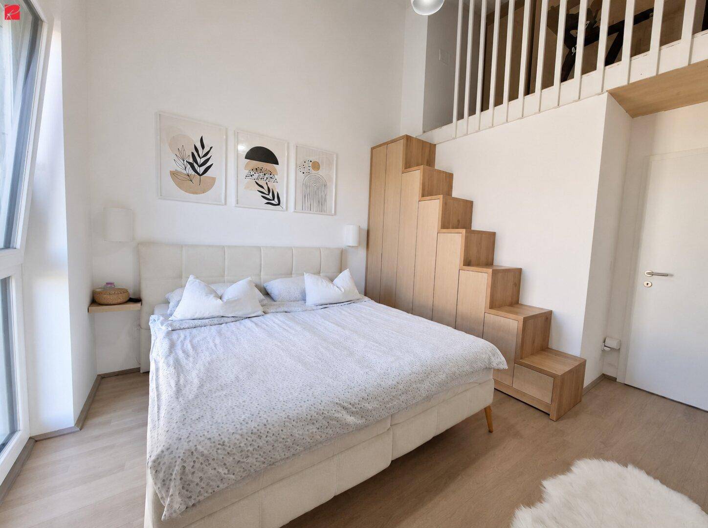 Helles Schlafzimmer mit großem Bett, minimalistischer Einrichtung und Holztreppe zu einer Galerie.