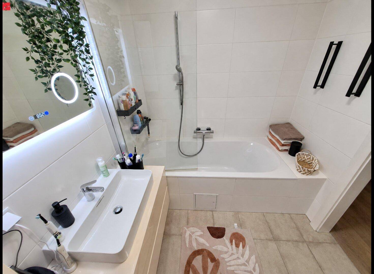 Modernes Badezimmer mit Badewanne, Dusche, Einzelwaschbecken und beleuchtetem Spiegel.