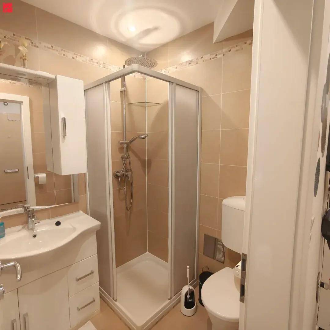 Badezimmer mit Duschkabine, Waschbecken und wandhängendem WC, gefliest in beigen Farbtönen.
