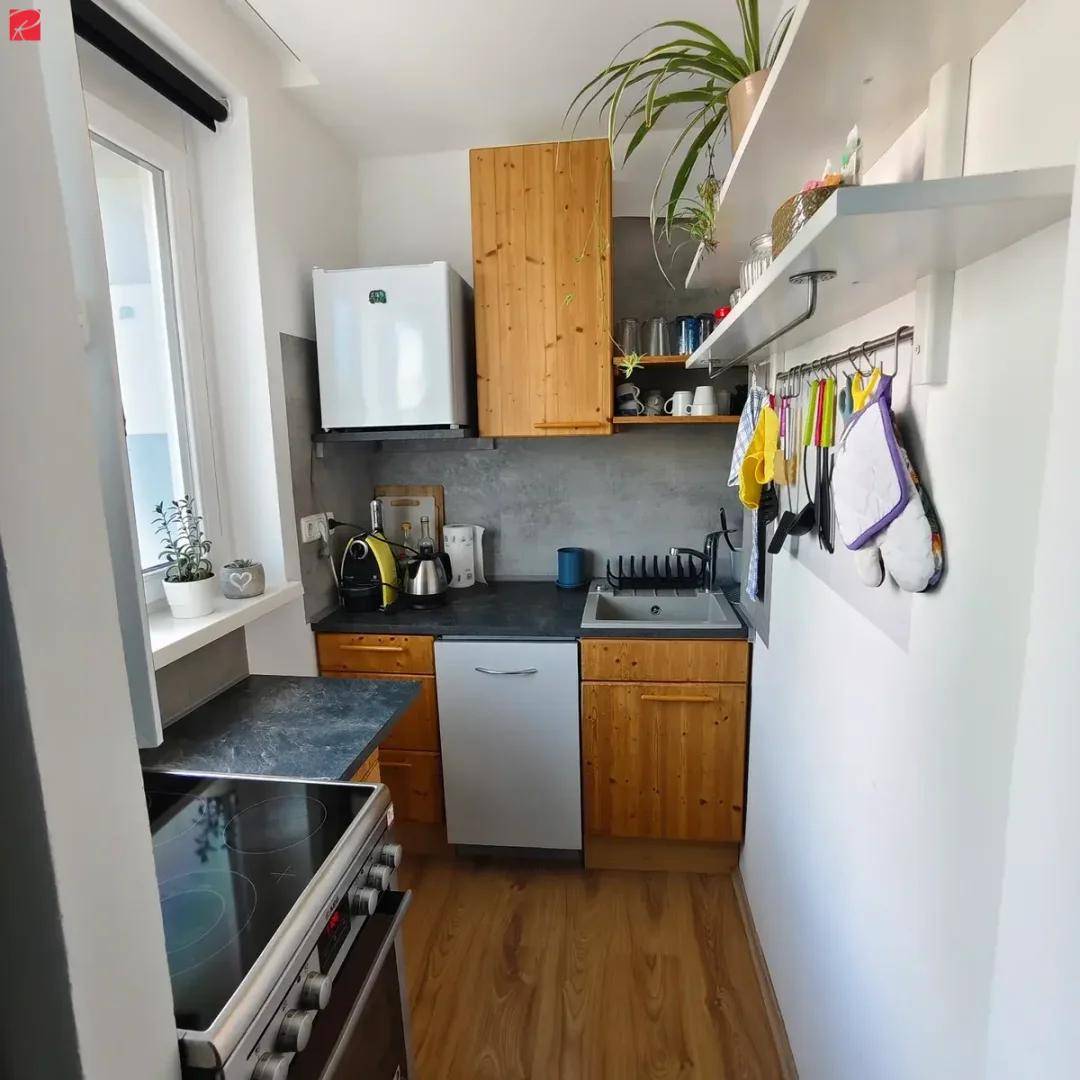 Kompakte Einbauküche mit Holzfronten, modernen Geräten und einem Fenster für Tageslicht.