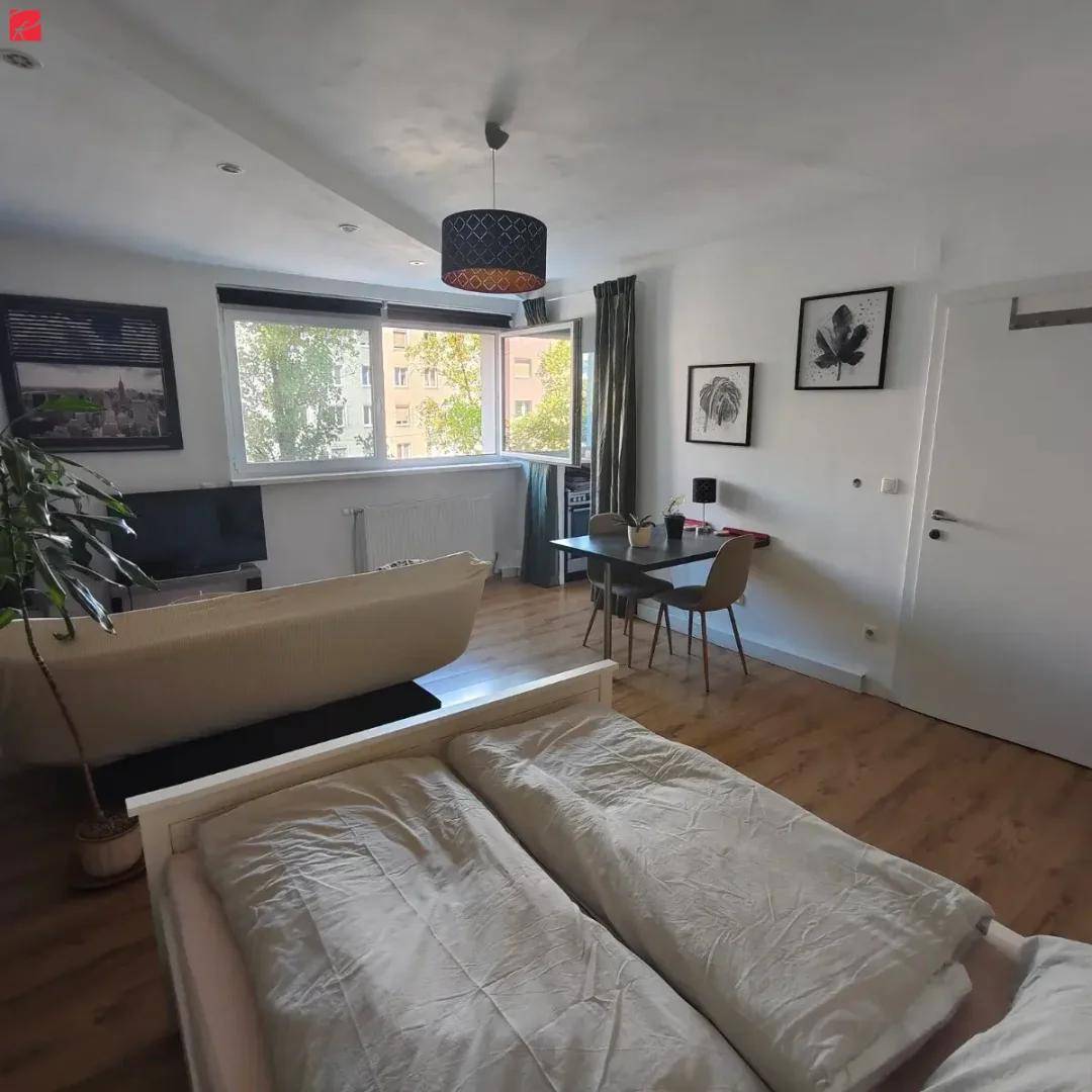 Heller Wohnbereich mit Bett, Sofa und kleinem Esstisch, ausgestattet mit Laminatboden und natürlichem Licht.