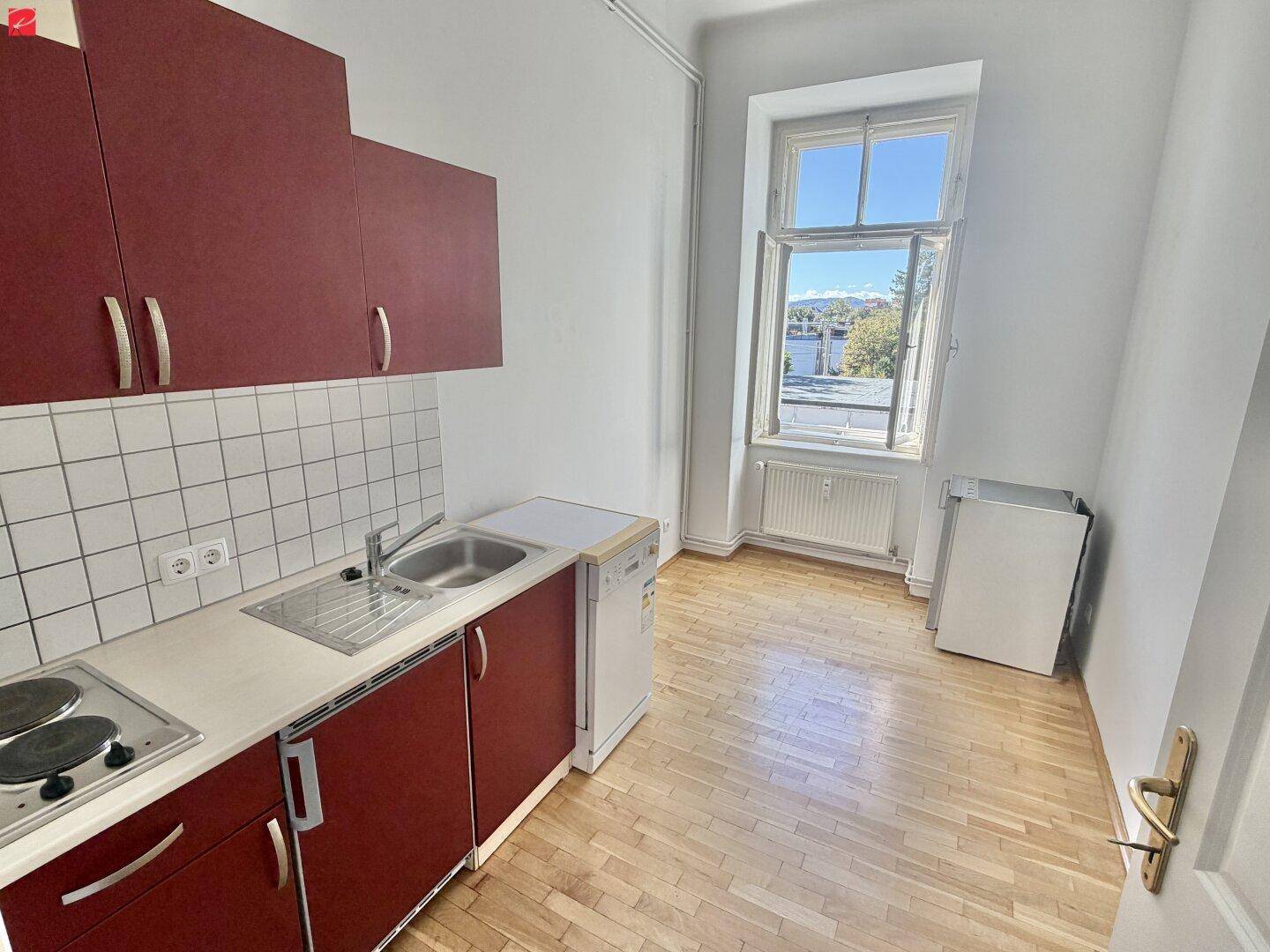 Funktionale Küche mit roten Schränken, Spüle, Kochfeld und Platz für einen kleinen Essbereich.