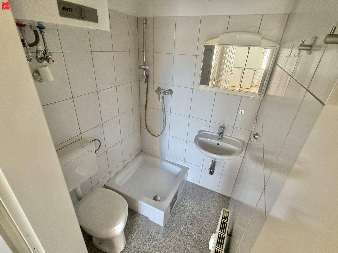 Kleines Badezimmer mit weißen Fliesen, Dusche, WC und Waschbecken mit Spiegelschrank.