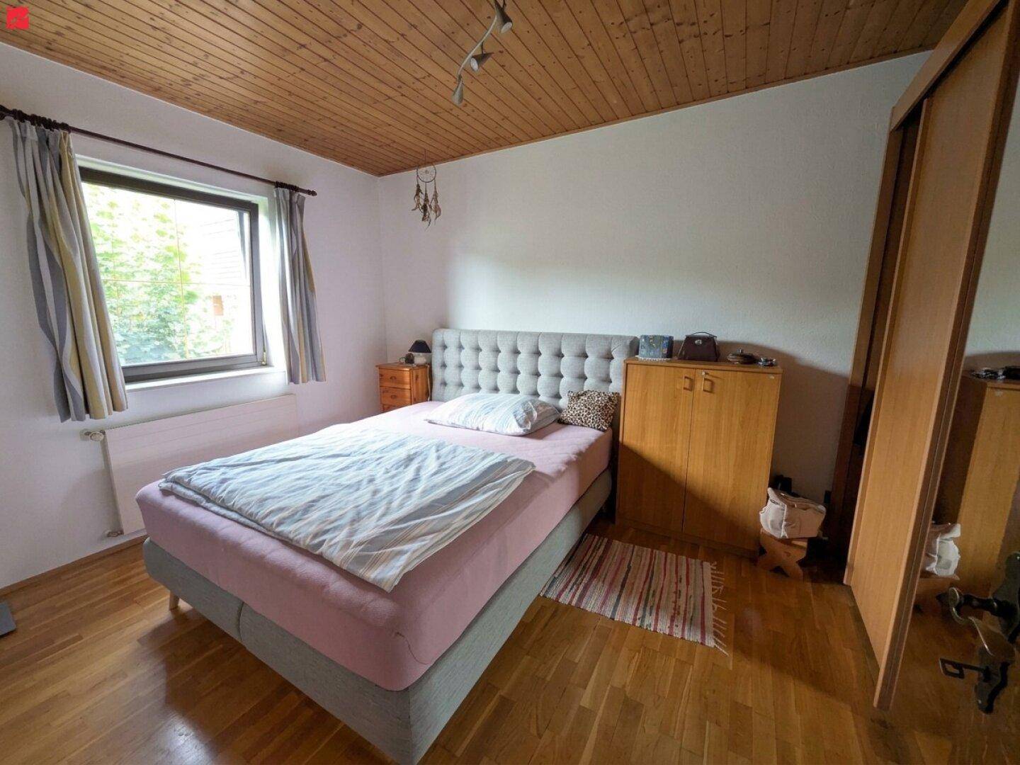 Schlafzimmer mit Doppelbett, Holzdecke, Parkettboden und großem Fenster für viel Tageslicht.
