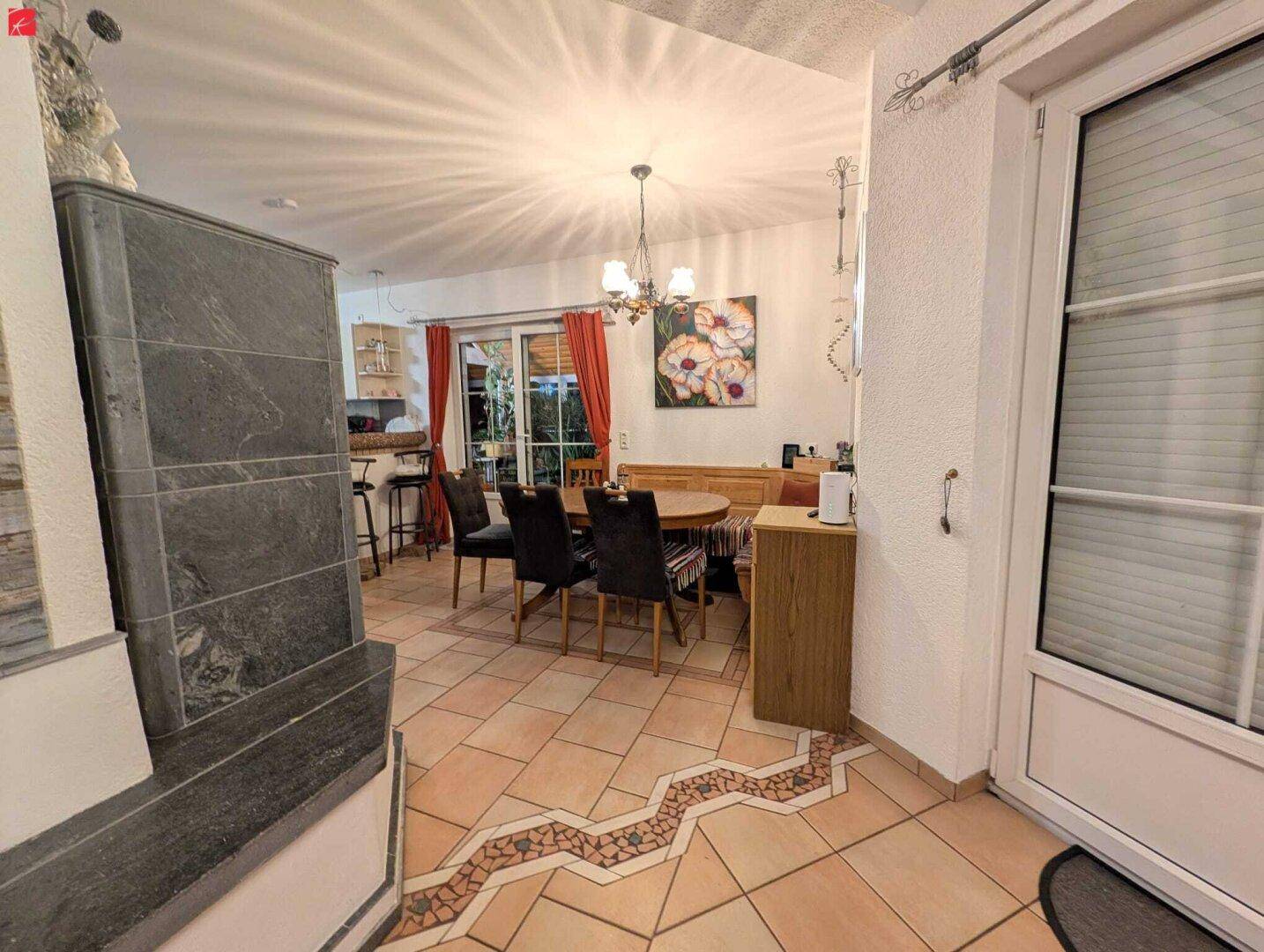 Gemütlicher Essbereich mit Kachelofen, Holztisch und Zugang zur Terrasse.