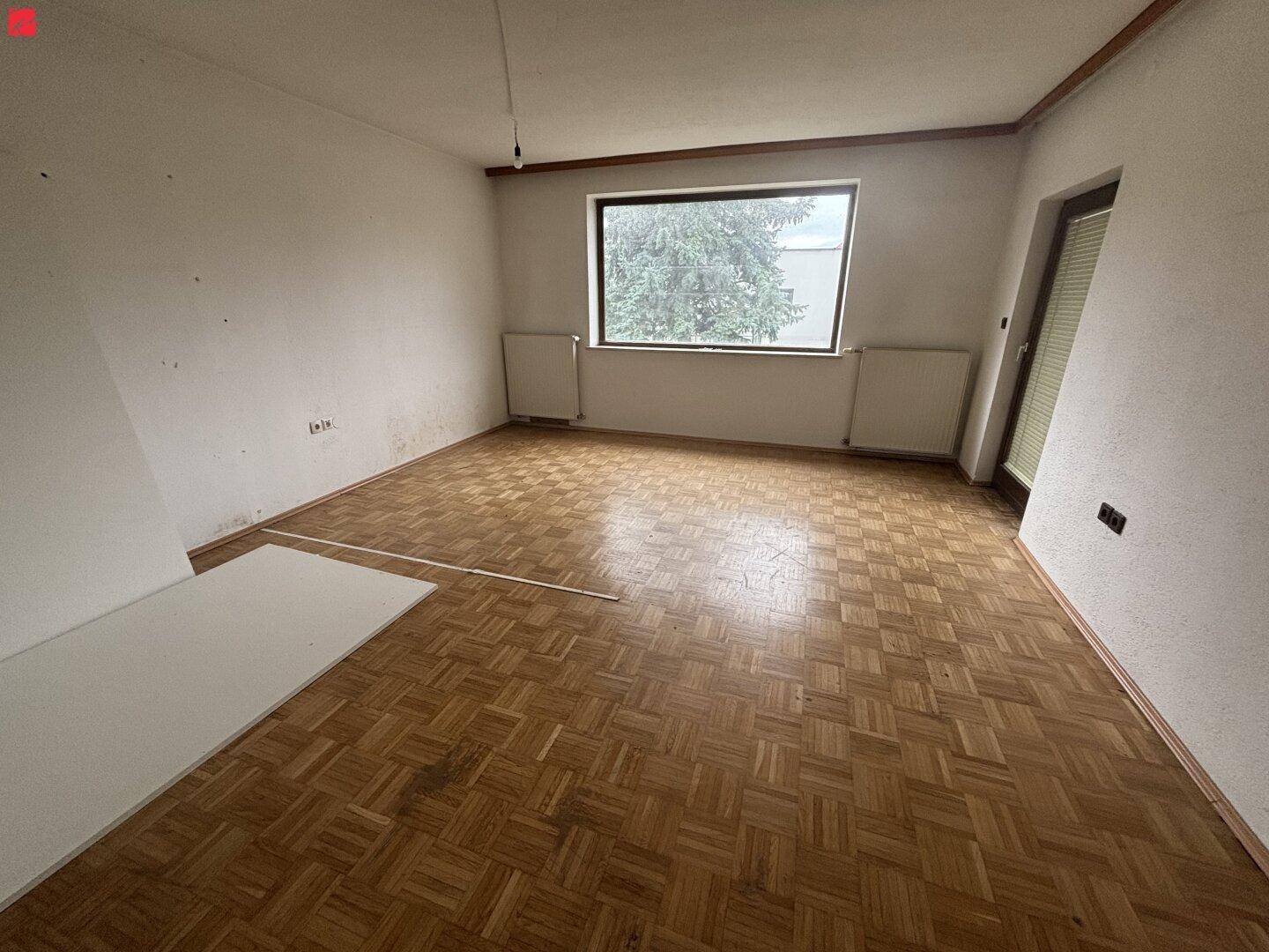 Leeres Zimmer mit Parkettboden und großem Fenster, bereit für die Renovierung.