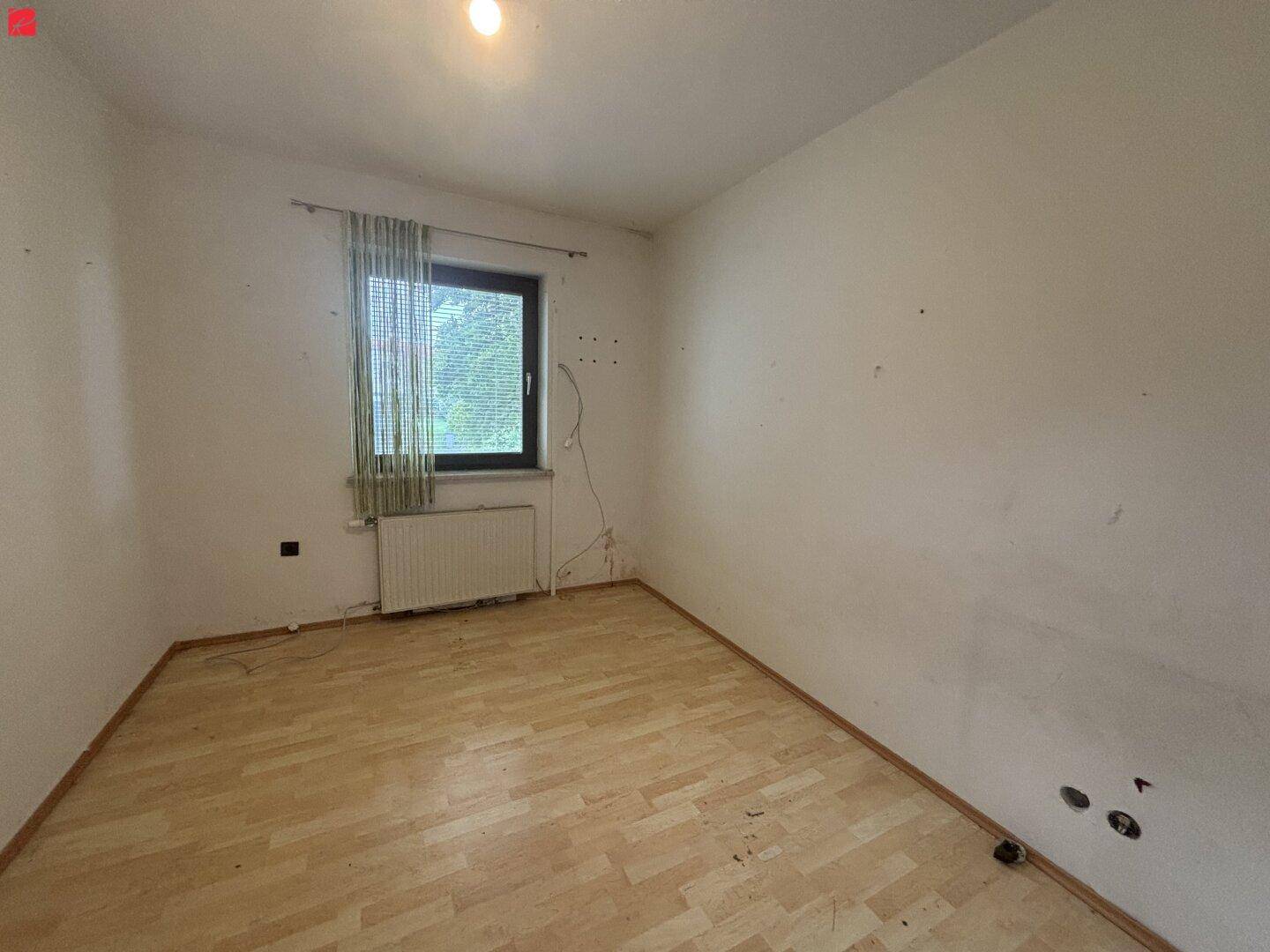 Helles Schlafzimmer mit Laminatboden und einem Fenster, das viel Tageslicht hereinlässt.