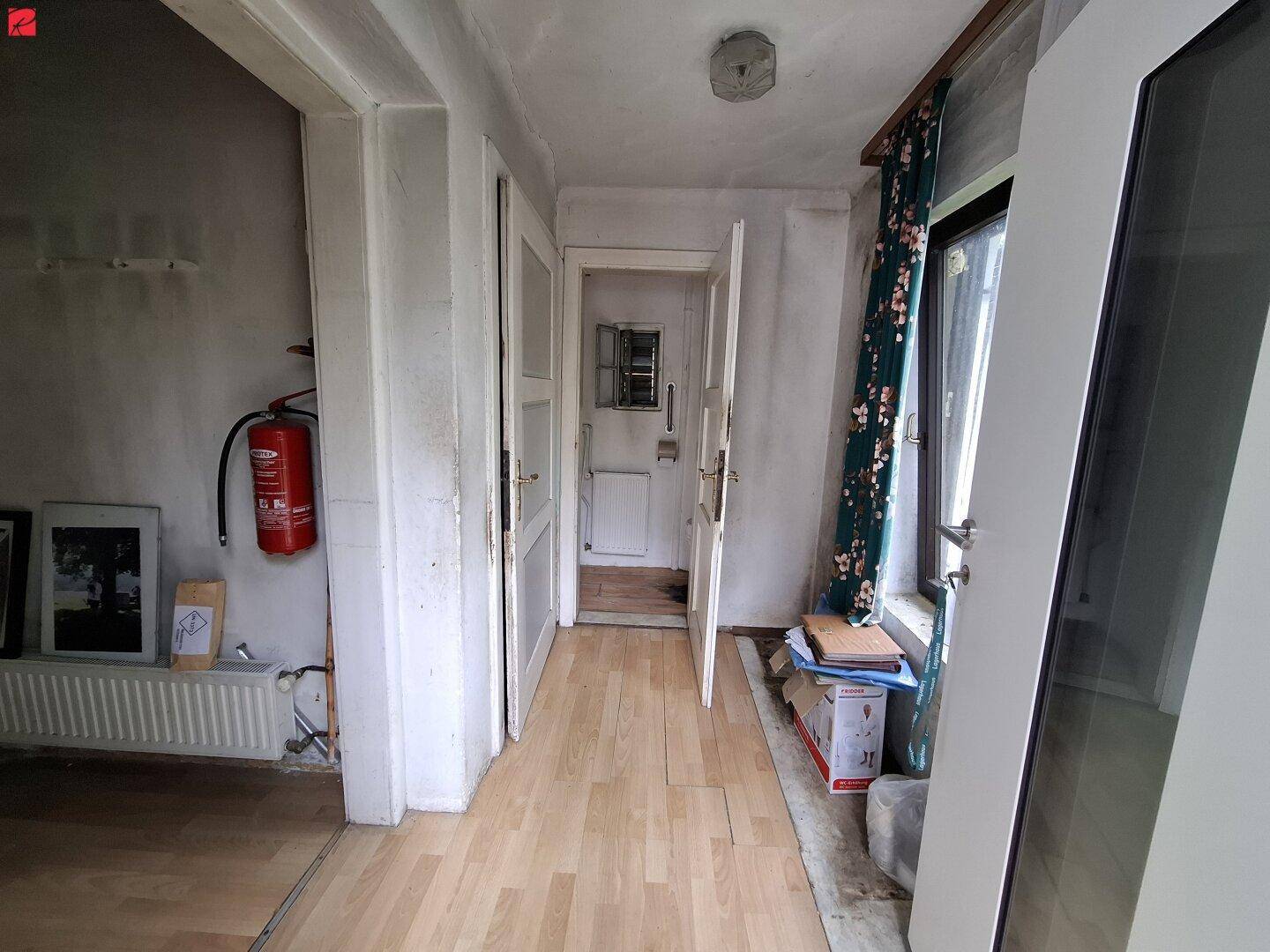 Langer Flur mit Holzboden und Türen zu weiteren Räumen, ausgestattet mit einem Feuerlöscher.